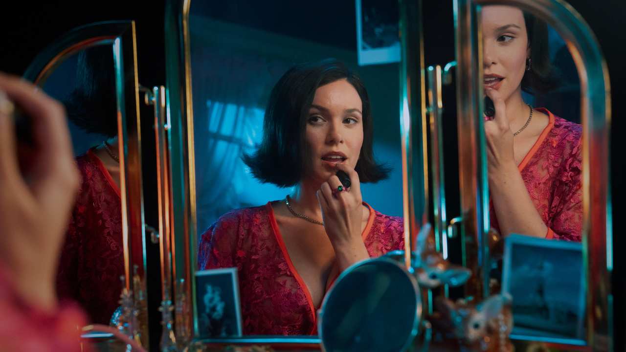 a woman putting on lipstick in front of a mirror